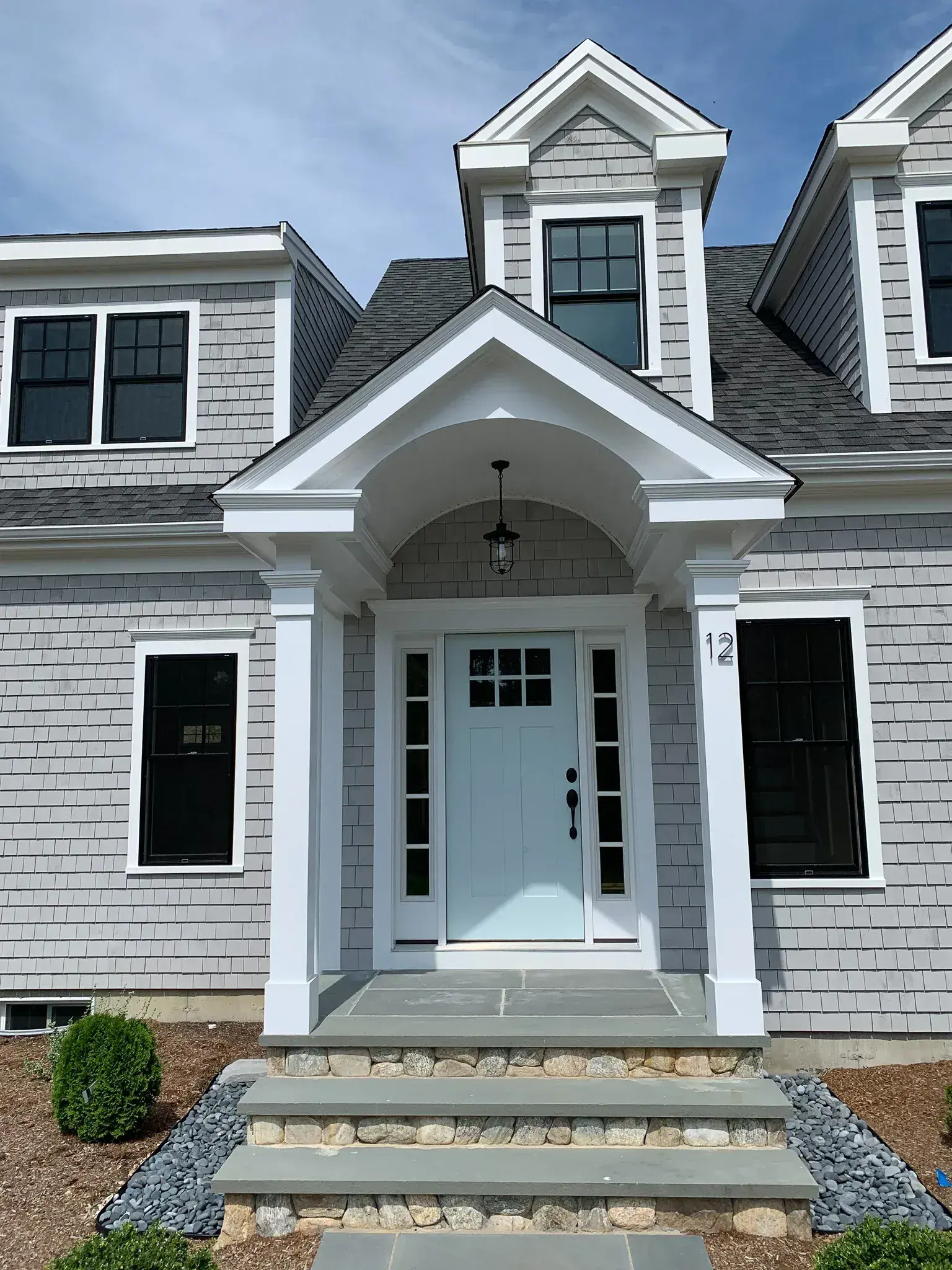Gray shingle front entry with arched portico and light blue door by Tuleika Building Company