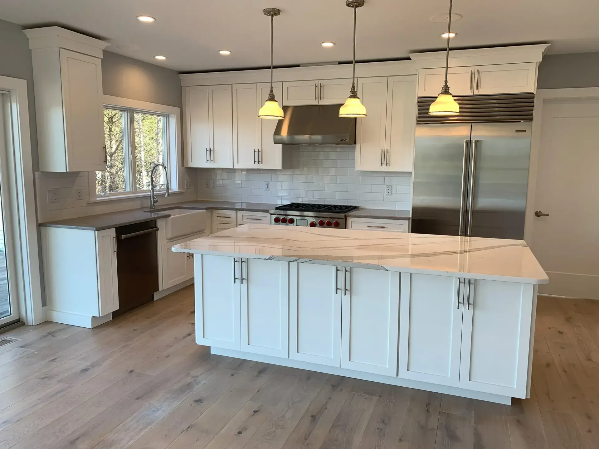 Renovated white kitchen with large island and pendant lighting on Cape Cod by Tuleika Building Company